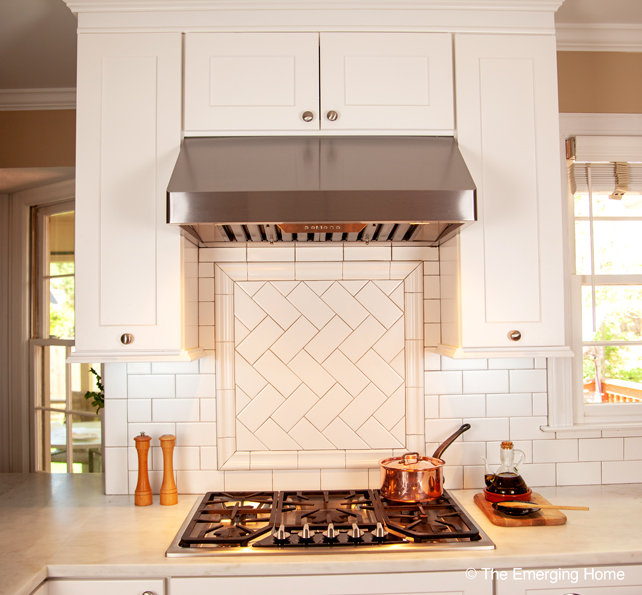 Stainless cooktop with exhaust fan above. Backsplash is square block of subway tile laid in a herringbone design.