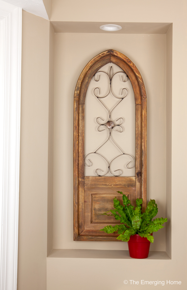 The natural wood art piece with a decorative metal inset hangs in the  niche in the kitchen. A red planter holds a small houseplant.