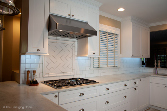 Long counter of top and lower white kitchen cabinets topped with marble. Electrical outlets are placed under top cabinets in order to allow uninterrupted subway tile backsplash. 