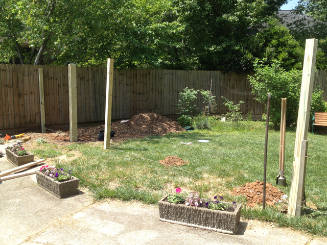 Fence posts are leaning in freshly dug holes in the area in front of driveway