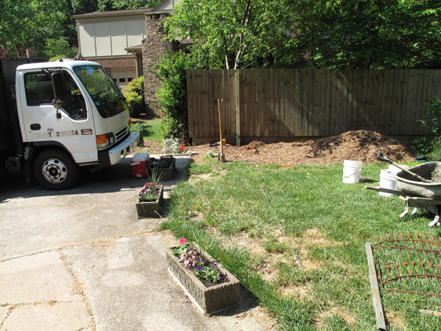 Yard area just in front of driveway is being prepared for installing of a picket fence. A string is laid out to note post holes.