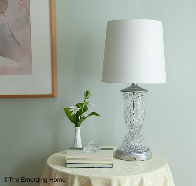 Updated crystal and glass table lamp with white drum shade sits on small table