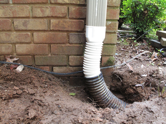 shows metal downspout above the downspout adapter that is now attached to the black flexible drainpipe that leads into the ground
