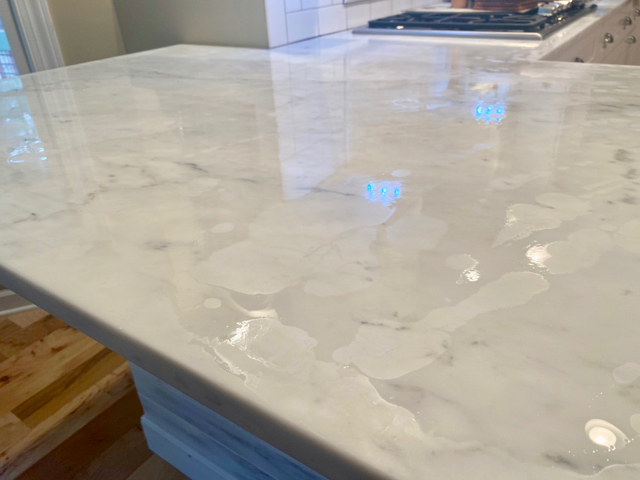 White marble countertop has liquid sealant on it with random light patches indicating areas of  absorption 