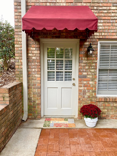 cleaned, red awning over door with colorful welcome mat and to of red mums