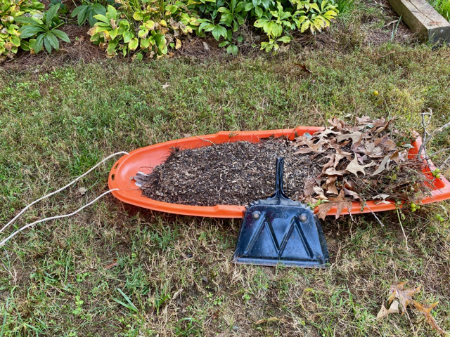 plastic snow sled is filled with old much, leaves and left over bird seed shells