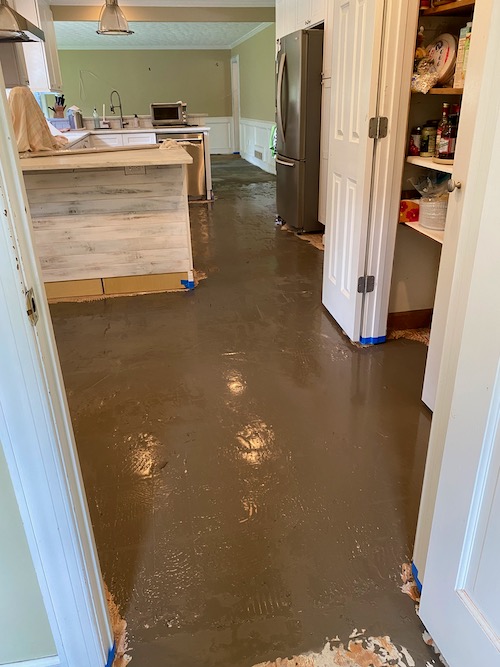 Dark grey concrete-like mixture is spread over floor for leveling before new floor is installed